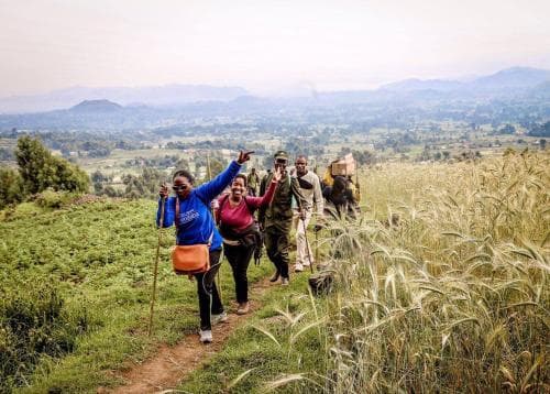 A joyful group hikes along a scenic dirt path through lush green fields, enjoying the expansive mountain views in a serene rural setting, perfect for adventure seekers looking to connect with nature.