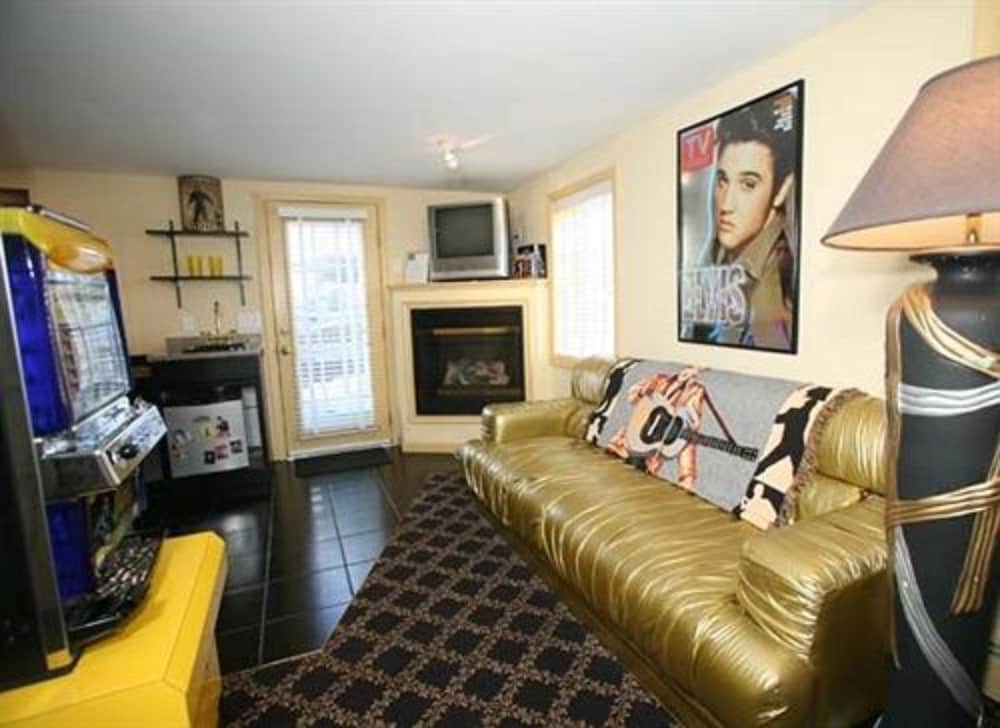 A cozy living room with a gold leather couch, Elvis Presley poster, vintage arcade machine, and fireplace creates a nostalgic and playful atmosphere ideal for a themed vacation rental.