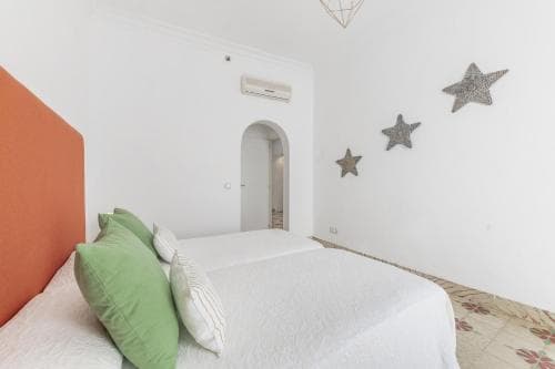 A cozy bedroom with a neatly made bed adorned with green and white pillows, an orange headboard, star decorations on the wall, and a tiled floor, ideal for travelers seeking a comfortable and charming accommodation.