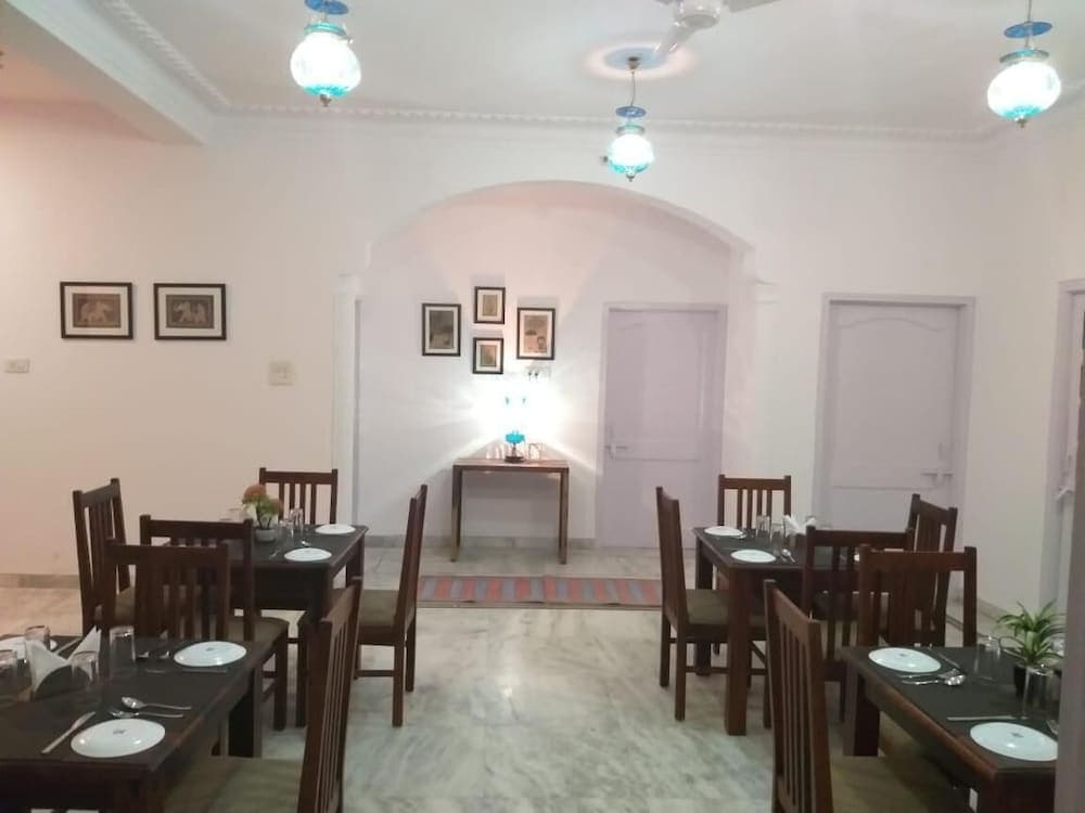 A cozy indoor dining area with marble floors, wooden tables set for meals, soft lighting from hanging lamps, framed artwork on the walls, and an inviting atmosphere perfect for travelers seeking a comfortable restaurant experience.