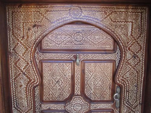 An intricately carved wooden door adorned with geometric patterns and a brass knocker exudes cultural richness, ideal for travelers exploring historic sites or seeking unique architectural details.