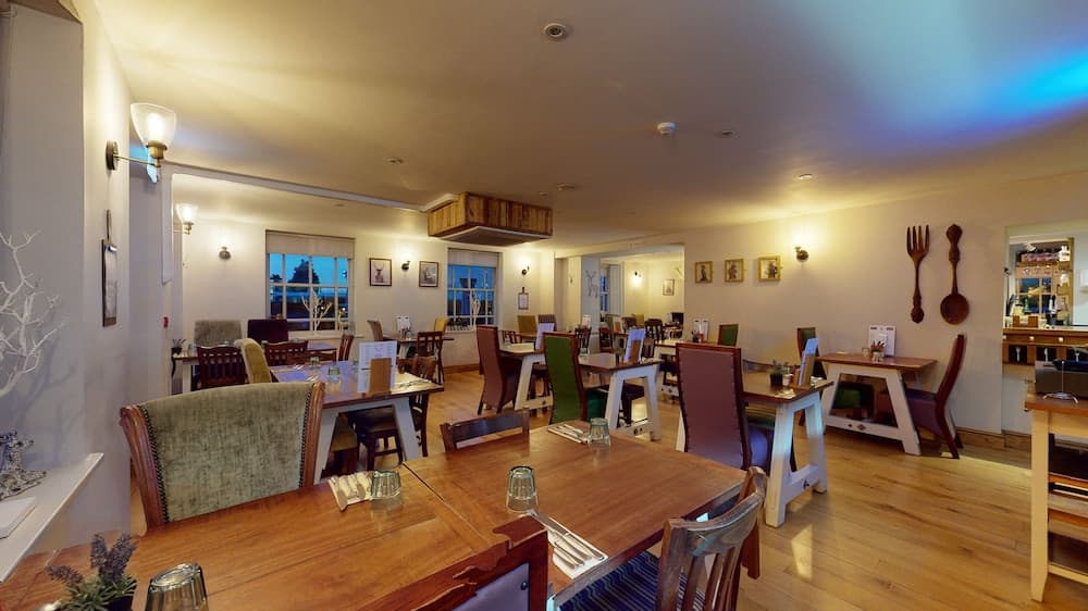 A cozy restaurant interior with wooden tables, eclectic chairs, warm lighting, and wall-mounted decor creates an inviting atmosphere ideal for travelers seeking a comfortable dining experience.