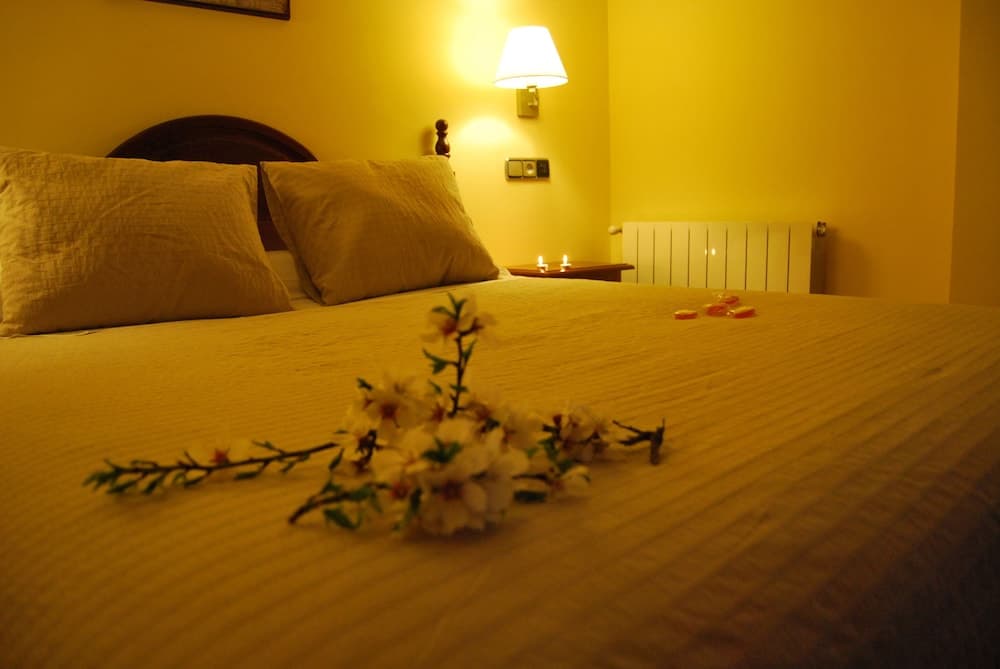 A cozy hotel room with warm yellow walls, a neatly made bed adorned with flowers, soft lighting, and romantic candles creates an inviting atmosphere perfect for a relaxing getaway.