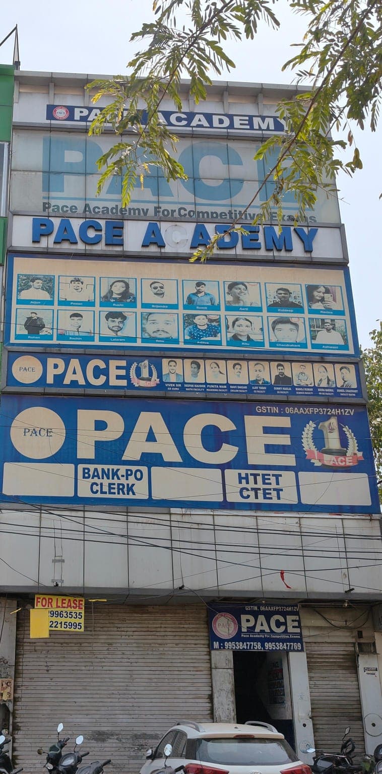 A bustling urban scene showcases the Pace Academy building in Gurugram, featuring prominent signage for competitive exam coaching, surrounded by parked vehicles and overhanging tree branches, ideal for travelers seeking educational services in India.