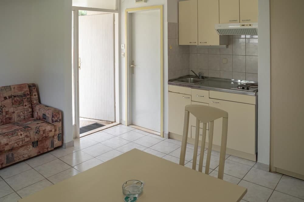 A cozy studio apartment features a compact kitchenette, tiled flooring, a patterned sofa, and an open doorway leading to natural light, ideal for budget-friendly travelers seeking a functional living space.