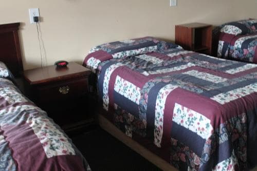 A cozy motel room features two beds adorned with floral-patterned quilts, a wooden nightstand with a clock, and a warm, inviting atmosphere ideal for budget travelers seeking comfort.