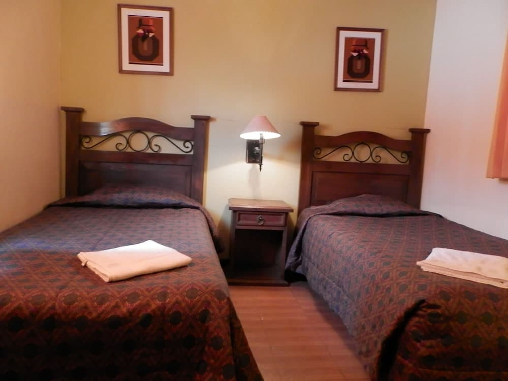 A cozy hotel room features two neatly made beds with patterned bedding, framed artwork on the walls, and a warm ambiance ideal for travelers seeking comfort and simplicity.