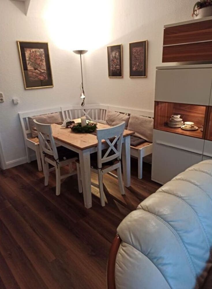 A cozy dining nook with wooden floors, white furniture, festive decorations, and warm lighting creates an inviting atmosphere ideal for travelers seeking a comfortable and homely accommodation experience.