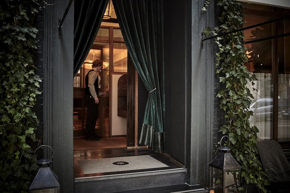 A cozy entrance to an upscale urban restaurant features lush ivy, elegant green curtains, and vintage lanterns, inviting travelers seeking a sophisticated dining experience.