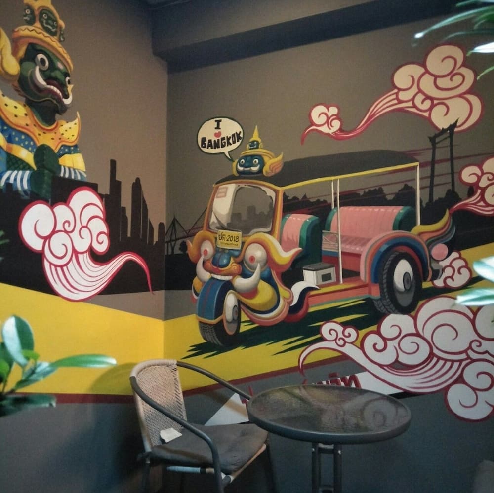 A vibrant mural featuring a whimsical tuk-tuk and traditional Thai elements creates a playful atmosphere in an indoor café setting, perfect for travelers seeking cultural inspiration and unique photo opportunities.