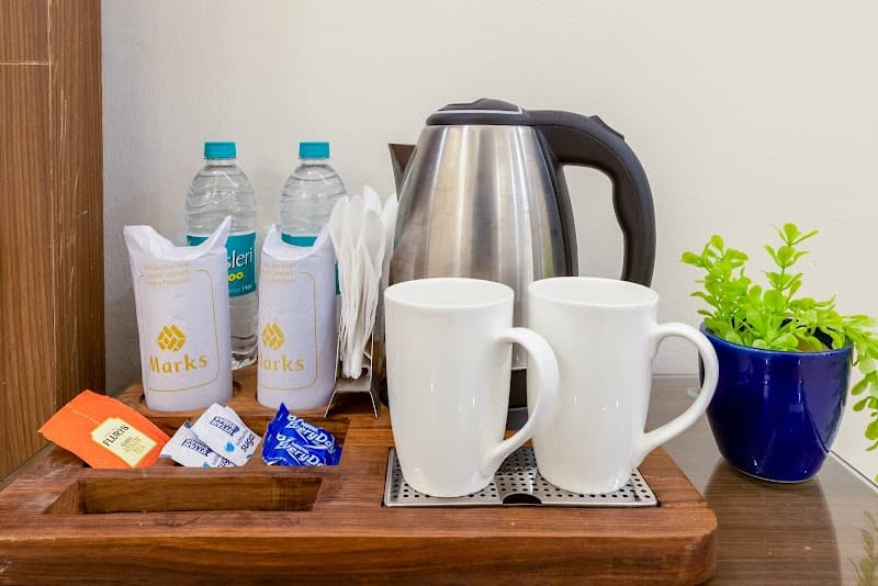 A cozy hotel room setup featuring a wooden tray with a kettle, two white mugs, bottled water, tea bags, and a small potted plant, ideal for travelers seeking comfort and convenience at Marks hotel in Noida, India.