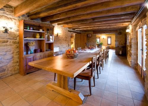 A cozy rustic dining area with stone walls, wooden beams, and long tables set for a warm gathering, ideal for travelers seeking a traditional countryside retreat experience.