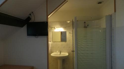 A cozy attic bathroom with a sloped ceiling, modern shower, pedestal sink, and wall-mounted TV, ideal for travelers seeking compact yet functional accommodations.