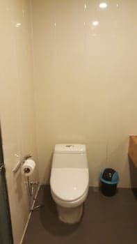 A clean, modern restroom with white walls, a toilet, a small trash bin, and a toilet paper holder creates a minimalist and functional space ideal for travelers seeking basic amenities in compact accommodations.