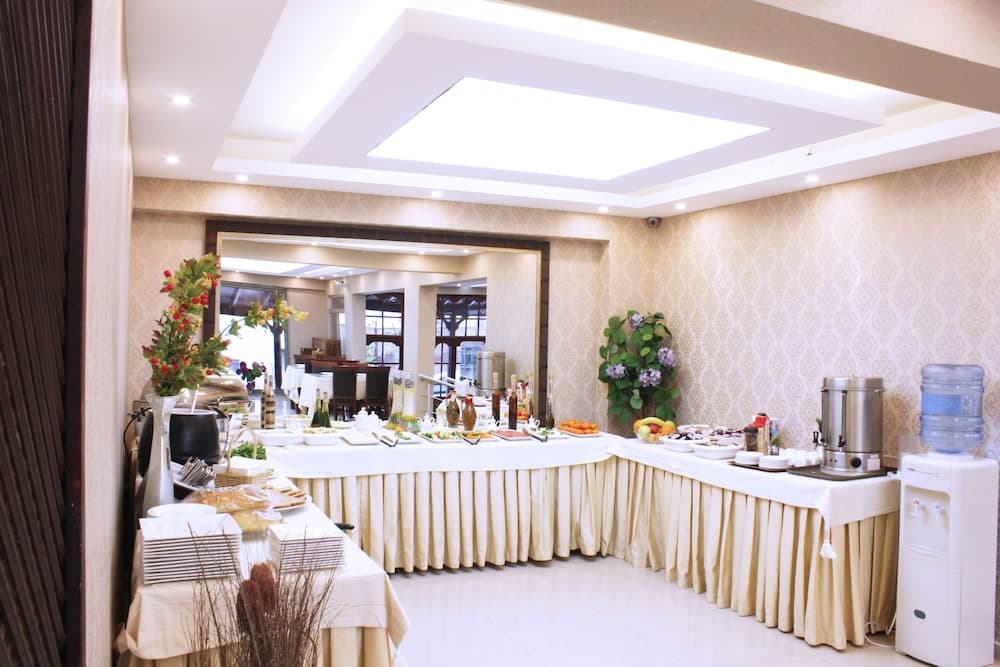 A warmly lit indoor buffet area with elegant decor, featuring a long table laden with food, beverages, and decorative plants, ideal for travelers seeking a comfortable dining experience in a hotel or conference setting.