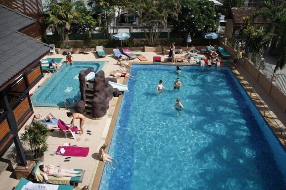 A vibrant tropical resort scene features a large pool surrounded by lounging guests, palm trees, and shaded cabanas, ideal for a relaxing vacation getaway.
