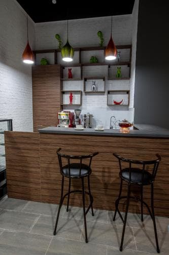 A cozy modern bar corner with sleek wooden counter, stylish black stools, and vibrant hanging lights creates an inviting atmosphere perfect for intimate gatherings or casual dining experiences.