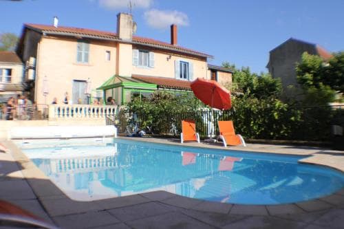 A serene outdoor poolside scene at a cozy villa features vibrant orange lounge chairs under a red umbrella, surrounded by lush greenery, ideal for relaxing summer getaways.