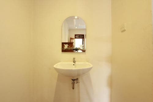 A minimalist bathroom features a white wall-mounted sink under an oval mirror, reflecting a cozy interior, ideal for travelers seeking simple accommodations.