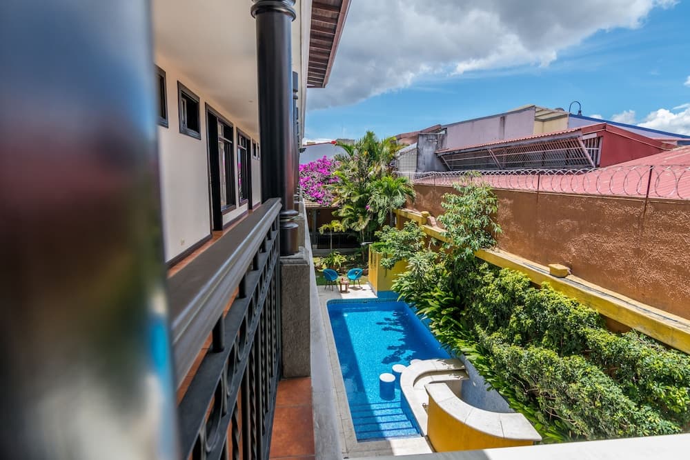 A serene balcony overlooks a vibrant tropical garden with a small pool, ideal for travelers seeking a peaceful retreat in an urban setting.