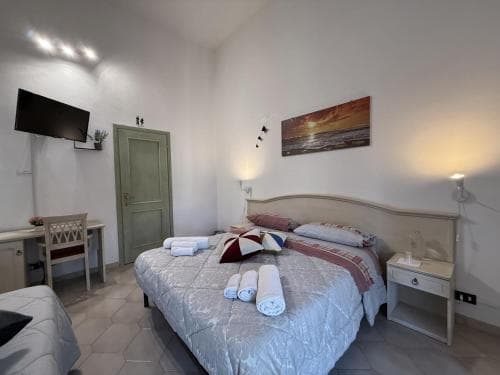 A cozy hotel room features a neatly made bed with colorful pillows, a desk by the door, warm lighting, and a serene sunset painting, ideal for travelers seeking comfort and relaxation.