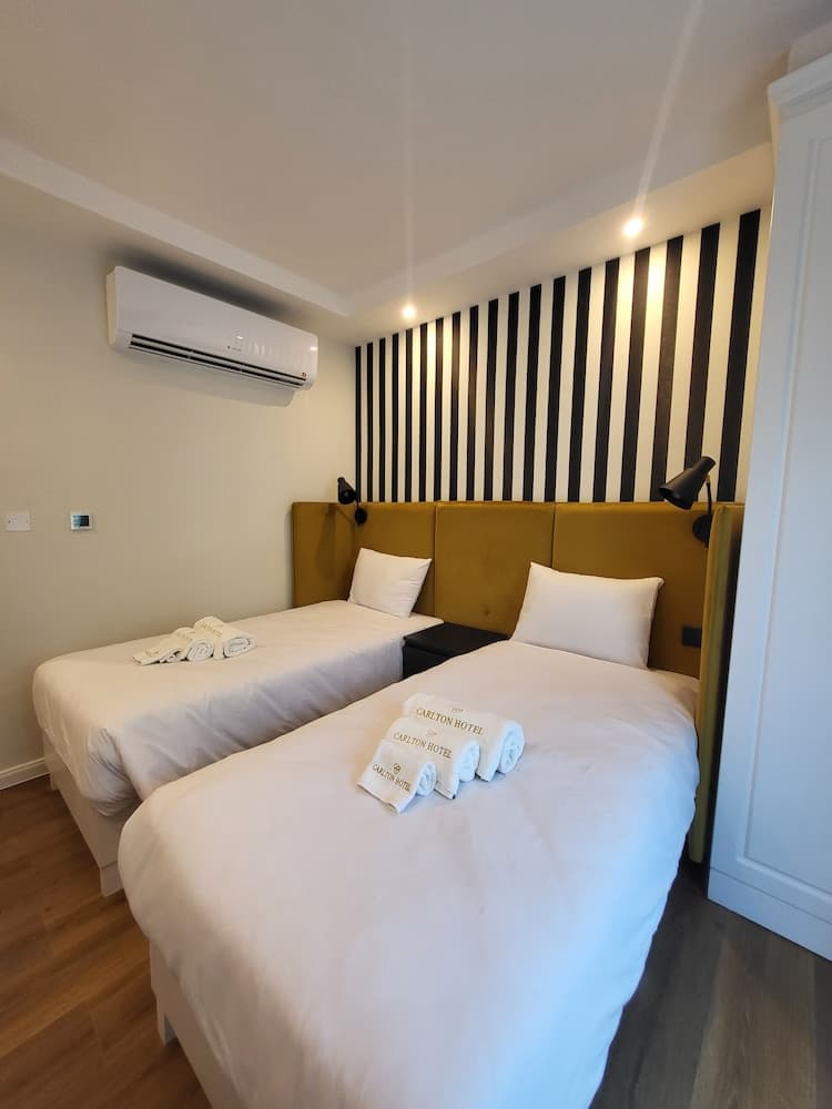 A cozy hotel room features two neatly made beds with white linens, a mustard-colored headboard, and a stylish black-and-white striped accent wall, ideal for travelers seeking comfort and modern design.