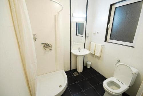 A compact hotel bathroom features a corner shower, pedestal sink, toilet, and frosted window, offering a clean and functional space for travelers seeking basic amenities.