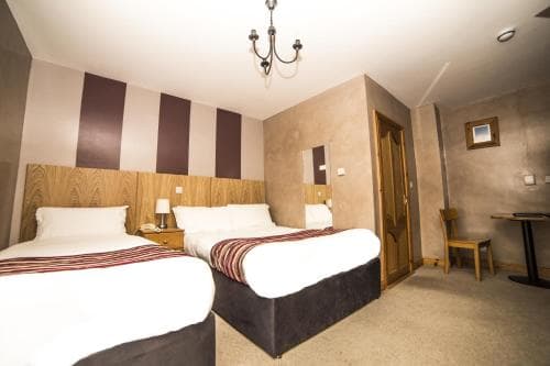 A cozy hotel room features two neatly made beds with striped runners, a wooden headboard, and warm lighting from a chandelier, creating an inviting atmosphere ideal for travelers seeking comfort and relaxation.