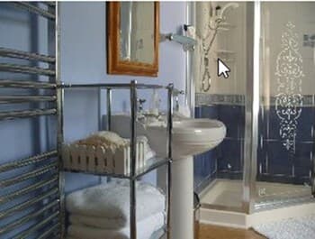 A cozy bathroom with blue walls, a white pedestal sink, a glass shower with decorative patterns, and neatly folded towels on shelves exudes a serene and inviting atmosphere, perfect for travelers seeking relaxation and comfort.