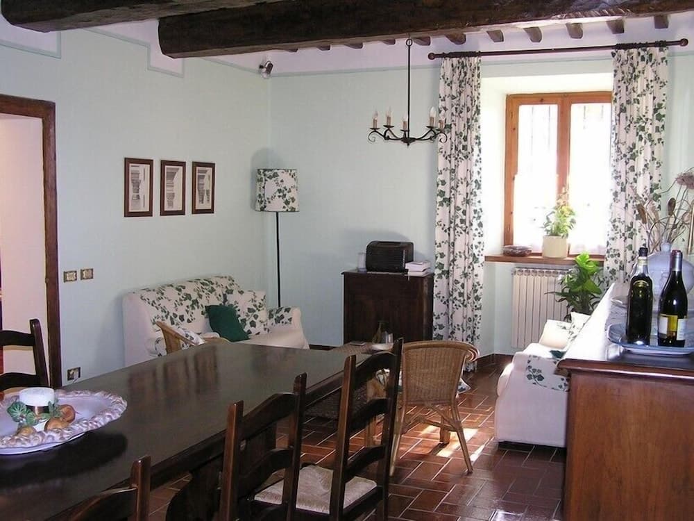 A cozy living room with rustic wooden beams, floral curtains, and a warm ambiance invites travelers seeking a charming countryside retreat, perfect for relaxing with a glass of wine by the window.