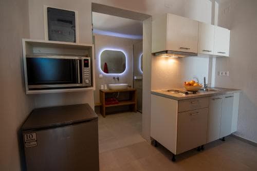 A cozy studio apartment features a compact kitchenette with white cabinets, a microwave, and a small fridge, leading to a bathroom with a lit mirror, ideal for travelers seeking convenience in urban accommodations.