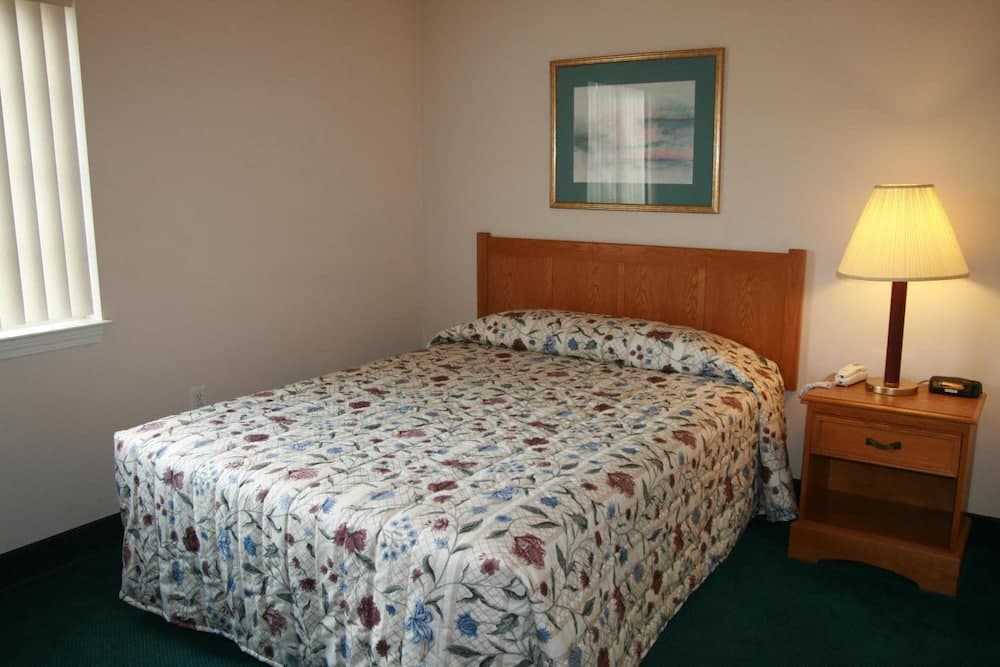 A cozy hotel room features a neatly made bed with a floral quilt, a wooden nightstand with a lamp, and a framed picture above the bed, ideal for travelers seeking comfort and simplicity.