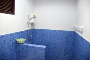 A serene, modern bathroom with blue textured walls, a built-in bench, and a handheld showerhead offers a tranquil space for relaxation, ideal for travelers seeking comfort in accommodations.
