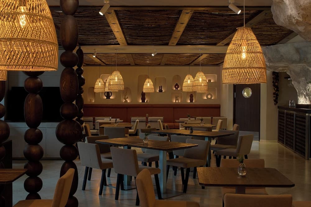 A cozy restaurant with rustic wooden ceilings, woven pendant lights, and modern furnishings creates an inviting atmosphere perfect for travelers seeking a unique dining experience.