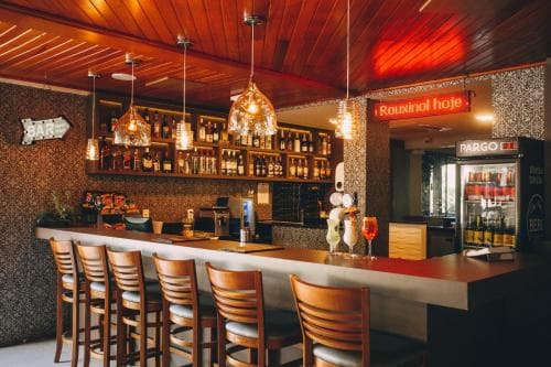 A cozy bar with warm wooden interiors, glowing pendant lights, and stocked shelves creates an inviting atmosphere perfect for travelers seeking a relaxing drink spot.
