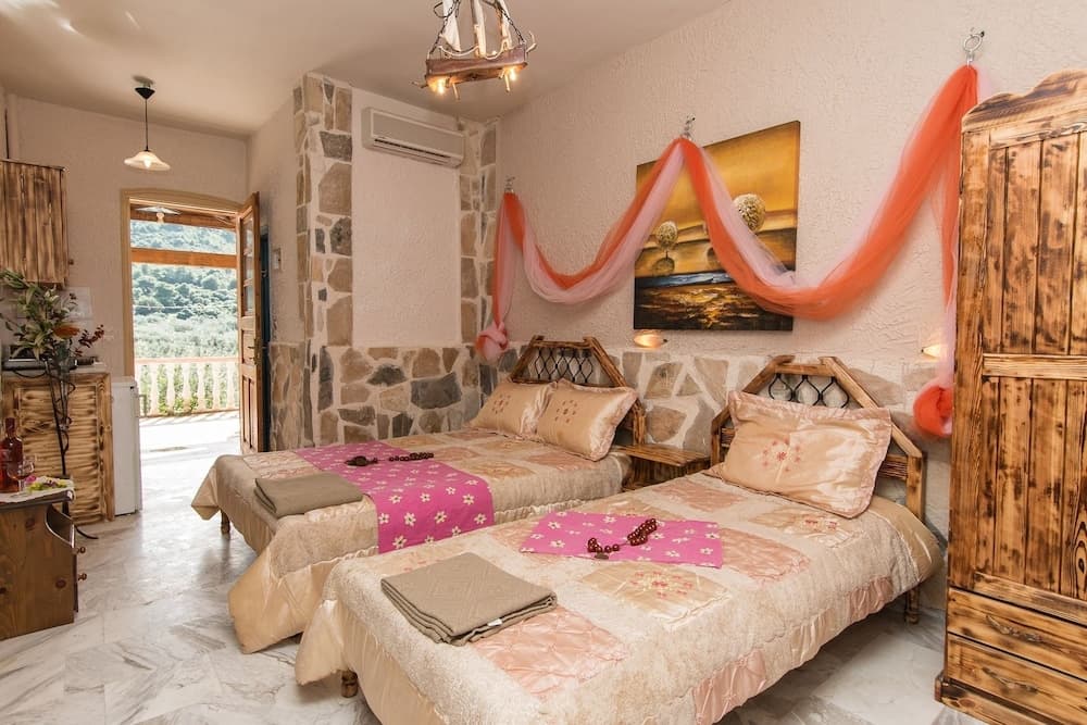 A cozy, rustic bedroom with twin beds adorned in floral linens, wooden furnishings, and a scenic balcony view, ideal for a tranquil countryside retreat.