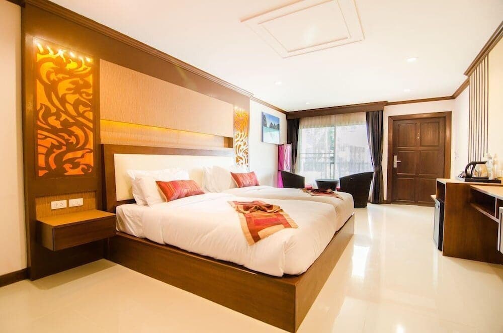 A cozy hotel room features two neatly made beds adorned with vibrant red accents, warm wooden furnishings, and decorative wall art, creating an inviting atmosphere ideal for travelers seeking comfort and relaxation.