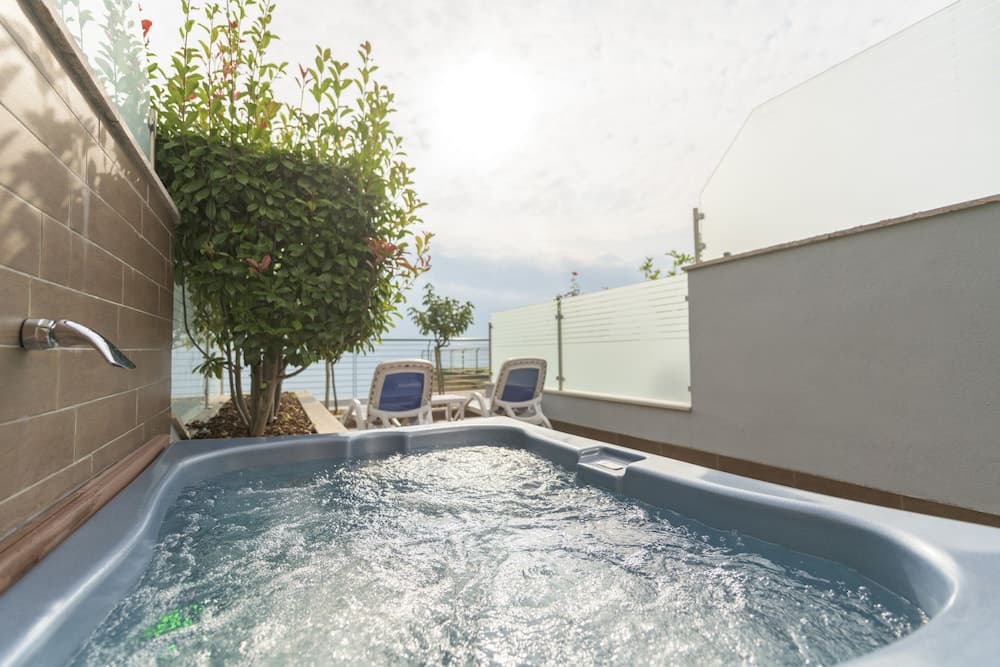 A serene rooftop retreat features a bubbling hot tub surrounded by lush greenery and lounge chairs, perfect for a relaxing vacation getaway.