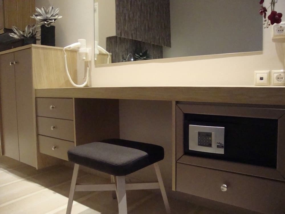 A modern hotel room desk setup features a sleek wooden desk with built-in drawers, a cushioned stool, decorative flowers, and an integrated safe, ideal for travelers needing a functional workspace in a cozy atmosphere.