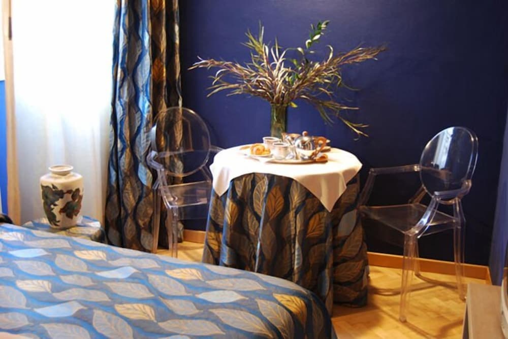A cozy hotel room features a vibrant blue wall, a table set with breakfast under a floral arrangement, transparent chairs, and patterned curtains, ideal for travelers seeking comfort and style.