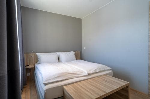 A cozy minimalist bedroom with a neatly made bed, wooden furniture, and soft lighting creates a serene atmosphere ideal for travelers seeking a peaceful retreat.
