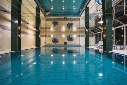 A serene indoor swimming pool with reflective blue tiles, modern lighting, and decorative wall art creates an inviting atmosphere ideal for relaxation and fitness activities.