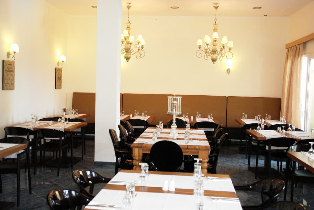 A cozy indoor restaurant with warmly lit chandeliers, neatly arranged tables set for dining, and cushioned seating offers an inviting atmosphere for travelers seeking a comfortable meal experience.