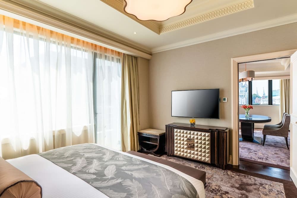 A luxurious hotel room features elegant decor with a cozy bed, stylish furniture, and large windows with sheer curtains, creating a serene atmosphere ideal for relaxation and leisure travel.