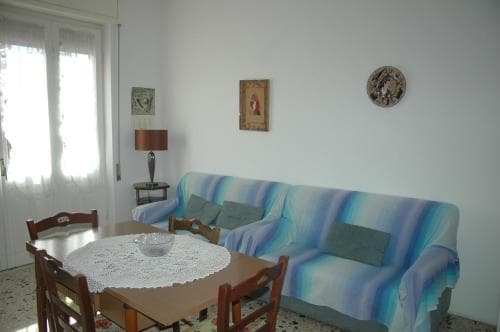 A cozy living room with a vibrant blue sofa, wooden dining set, and decorative wall art creates a welcoming atmosphere ideal for travelers seeking a comfortable apartment stay.