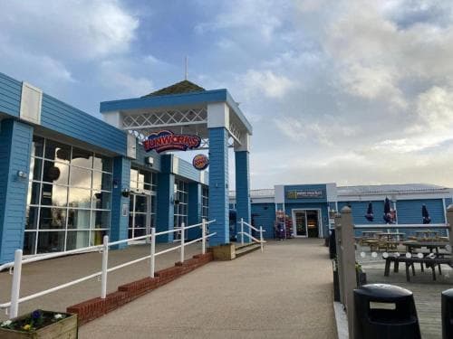 A vibrant blue-themed amusement arcade entrance under a partly cloudy sky invites visitors to enjoy family-friendly entertainment and games by the seaside.