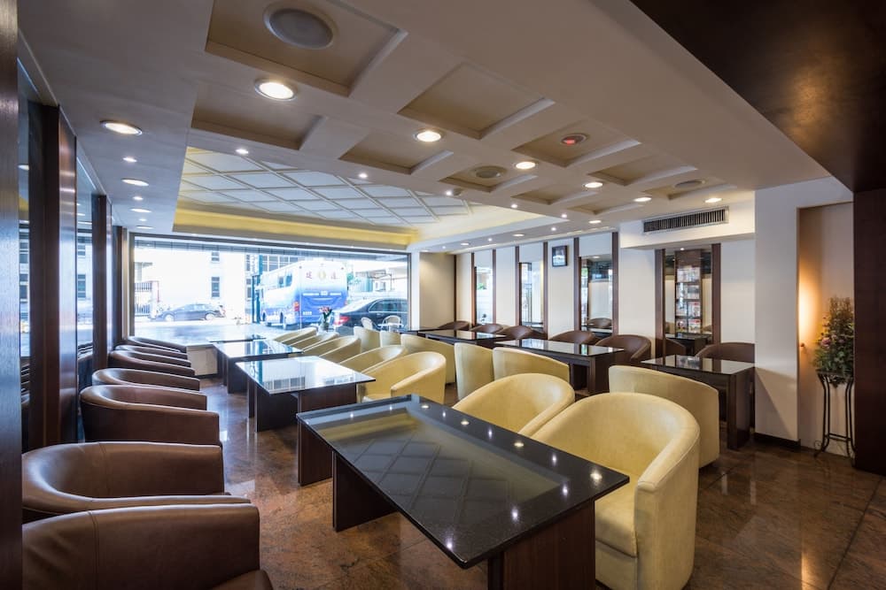 A cozy indoor lounge with plush armchairs, sleek tables, and large windows offering a view of the bustling street outside, ideal for travelers seeking a comfortable waiting area or meeting spot.