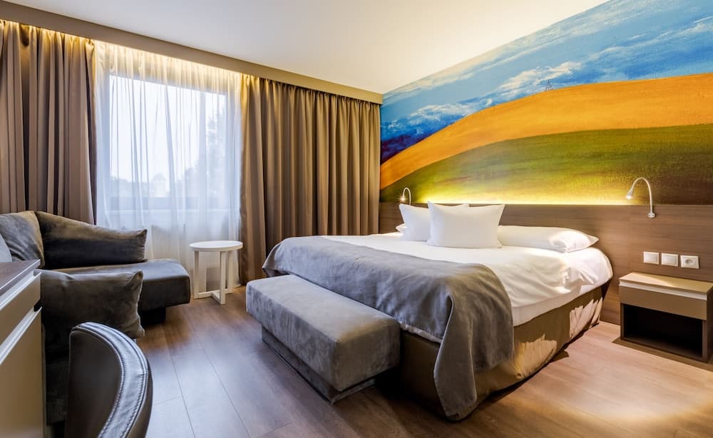 A cozy hotel room features a serene landscape mural, plush seating, and soft lighting, ideal for travelers seeking relaxation and comfort.