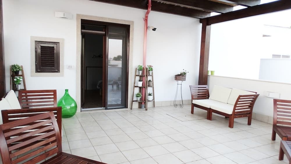 A serene tiled patio with wooden furniture, potted plants, and a glass door invites travelers to relax in a cozy outdoor living space.