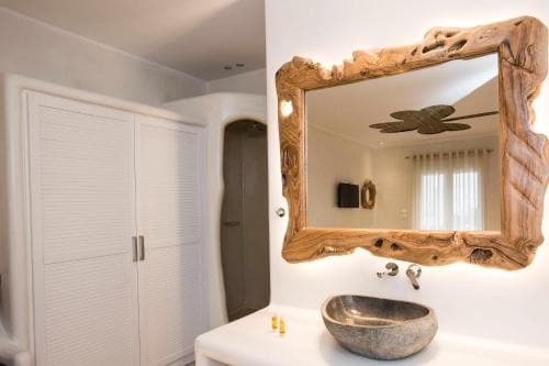 A serene bathroom features a rustic wooden-framed mirror above a stone sink, complemented by minimalist decor, ideal for travelers seeking a tranquil retreat experience.